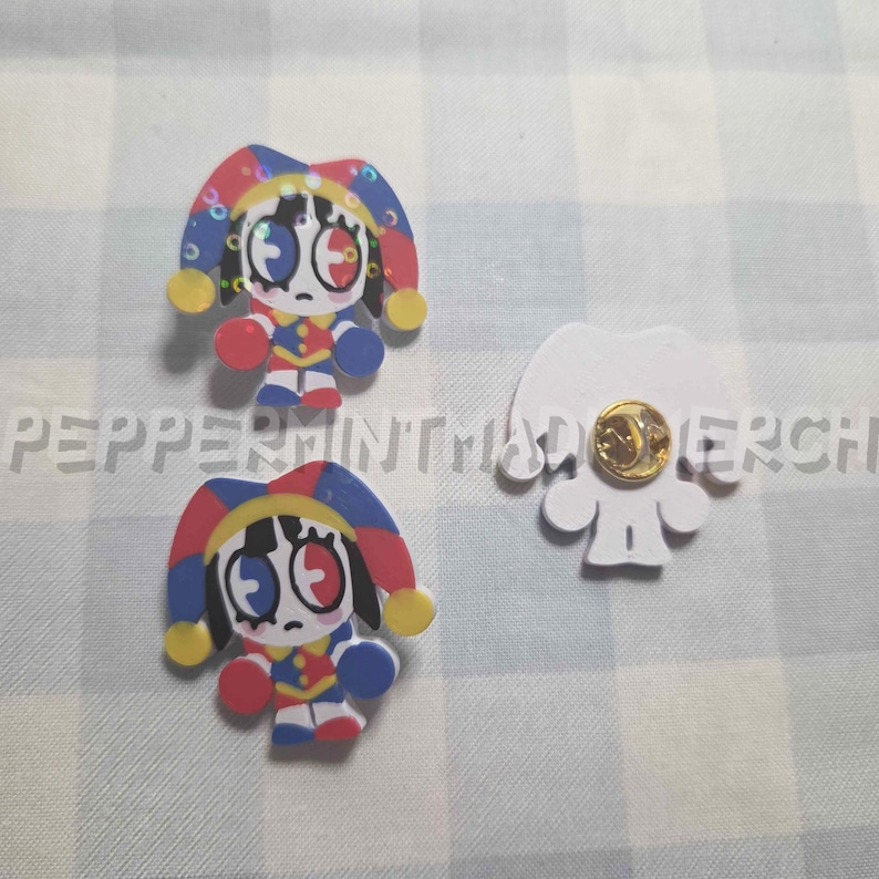 May include: Three decorative pins featuring a cartoon jester design. The jester pins have a red, blue, yellow, and white color scheme. One pin is a white silhouette with a gold pin back.