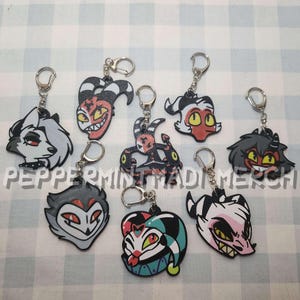 May include: A collection of character keychains with silver key rings and lobster claw clasps. The keychains feature various cartoon character designs in red, black, white, and yellow. The text "Peppermint Made Merch" is visible.
