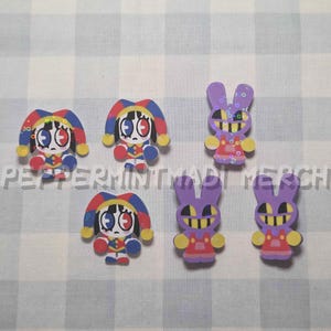 May include: A collection of colorful cartoon character pins. The pins feature a jester-like figure with red, blue, and yellow accents, and purple rabbit-like figures with yellow and red details. The text "PEPERMINTMADE MERCH" is visible.