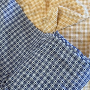 Peut inclure: Deux morceaux de tissu avec un motif à petits carreaux vichy. L'un est bleu foncé et blanc, tandis que l'autre est jaune pâle et blanc. Les deux tissus présentent un motif répétitif de minuscules cœurs à l'intérieur des petits carreaux.