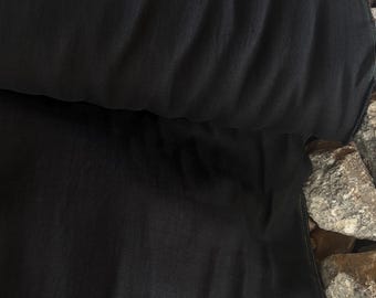 May include: A rolled-up length of black fabric, possibly linen or a similar material, with visible texture and folds. The fabric is a solid, deep black color. The edges of the fabric are visible, showing a clean, finished seam.