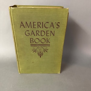 May include: A green hardcover book with the title "America's Garden Book" printed in brown lettering. The book has a decorative design on the front cover.