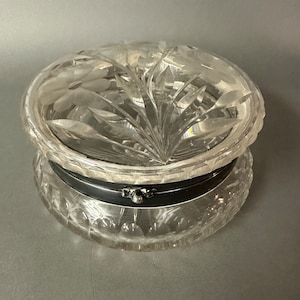 May include: A clear glass trinket box with a hinged lid. The lid and base are both cut with a floral design. The box has a silver metal hinge and clasp.