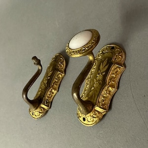 May include: Two ornate gold-toned hooks with decorative floral patterns. One hook has a white porcelain knob.