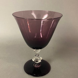 May include: A purple glass goblet with a clear glass stem and base. The goblet has a wide, flared bowl and a delicate, ornate stem.