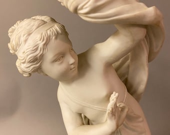 May include: A white porcelain figurine of a young woman with flowing drapery. The figurine is in a classical style and is likely from the 19th century.