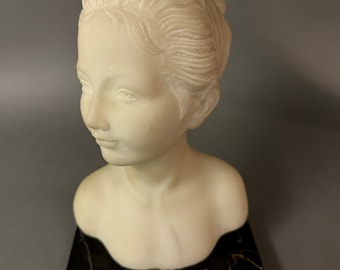 May include: White marble bust of a woman with her hair pulled back in a bun. The bust is on a black marble base.