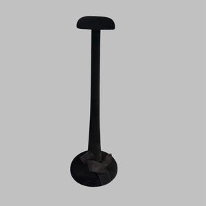 May include: A black hat display stand with a round base and a vertical stem. The top of the stand has a rounded, hat-shaped form. The stand is made of a dark material and is set against a neutral background.