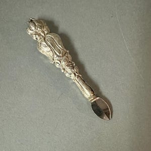 May include: A silver-colored butter knife with a floral design on the handle. The handle has a detailed, ornate pattern, and the blade is a simple, curved shape. The knife is likely made of metal.