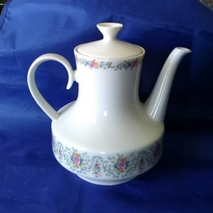 May include: White porcelain teapot with a floral design in shades of pink, blue, and green. The teapot has a lid and a handle.
