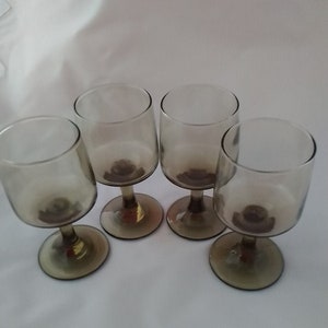 May include: Set of four clear glass wine glasses with a brown tint. The glasses have a round bowl and a stem.