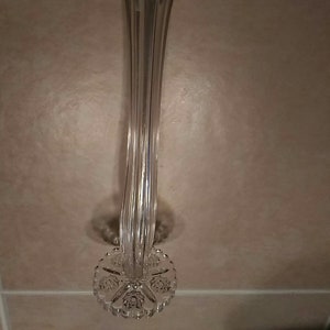 May include: A clear glass vase with a fluted design and a decorative base. The base is shaped like a flower with a scalloped edge.