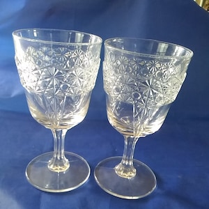 May include: Two clear glass wine glasses with a cut glass design. The glasses have a round bowl and a tall stem.