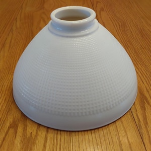 May include: A white, frosted glass lampshade with a textured surface. The shade is shaped like a cone and has a wide opening at the top.