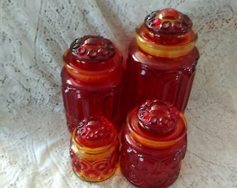 May include: Set of four red and amber glass canisters with starburst patterns. The canisters are of varying sizes and have a vintage look.