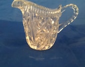 A clear glass creamer with deep wedges throughout with handle. Dish 561
