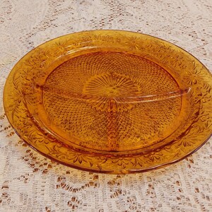 May include: Amber-colored, divided serving dish with a floral and geometric pattern. The round dish has three sections and a decorative rim. A vintage piece for serving snacks or appetizers.