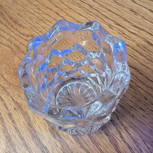 May include: A clear glass candle holder with a geometric design. The holder has a wide, open top and a narrow base.