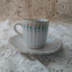 May include: A white teacup and saucer with a gold rim and a green, yellow, and red floral pattern.