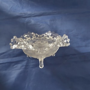 May include: A clear glass pedestal bowl with a scalloped edge and a three-legged base.