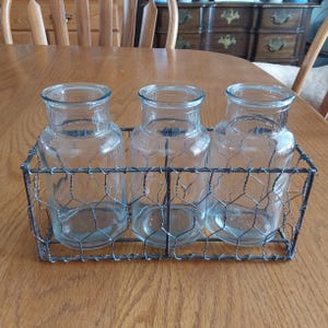 May include: Three clear glass jars in a wire mesh basket. The basket is made of a wire mesh with a hexagonal pattern. The jars are all the same size and shape.