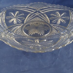 May include: Clear glass serving dish with a scalloped edge and intricate starburst and geometric patterns. The dish has a central circular design and is likely used for serving food or displaying decorative items.