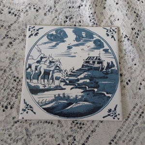 May include: A blue and white ceramic tile with a scene of animals and a building. The tile is decorated with a blue and white design. The animals are a horse, a donkey, and a dog. The building is a small house with a roof.