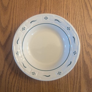 May include: A white ceramic bowl with a blue and green floral design around the rim. The bowl is empty and has a smooth, glossy finish.