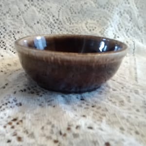 May include: A small brown ceramic bowl with a glazed finish. The bowl has a rounded shape and a slightly flared rim.