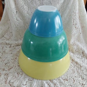 May include: A set of three vintage mixing bowls, nested together. The top bowl is blue, the middle bowl is green, and the bottom bowl is yellow.