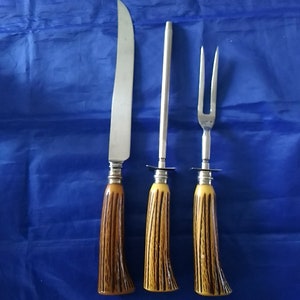 K&ouml;nnte beinhalten: Ein Set aus drei K&uuml;chenutensilien mit braunen und gelben Griffen. Das Set enth&auml;lt ein Messer, eine Fleischgabel und einen Wetzstahl.