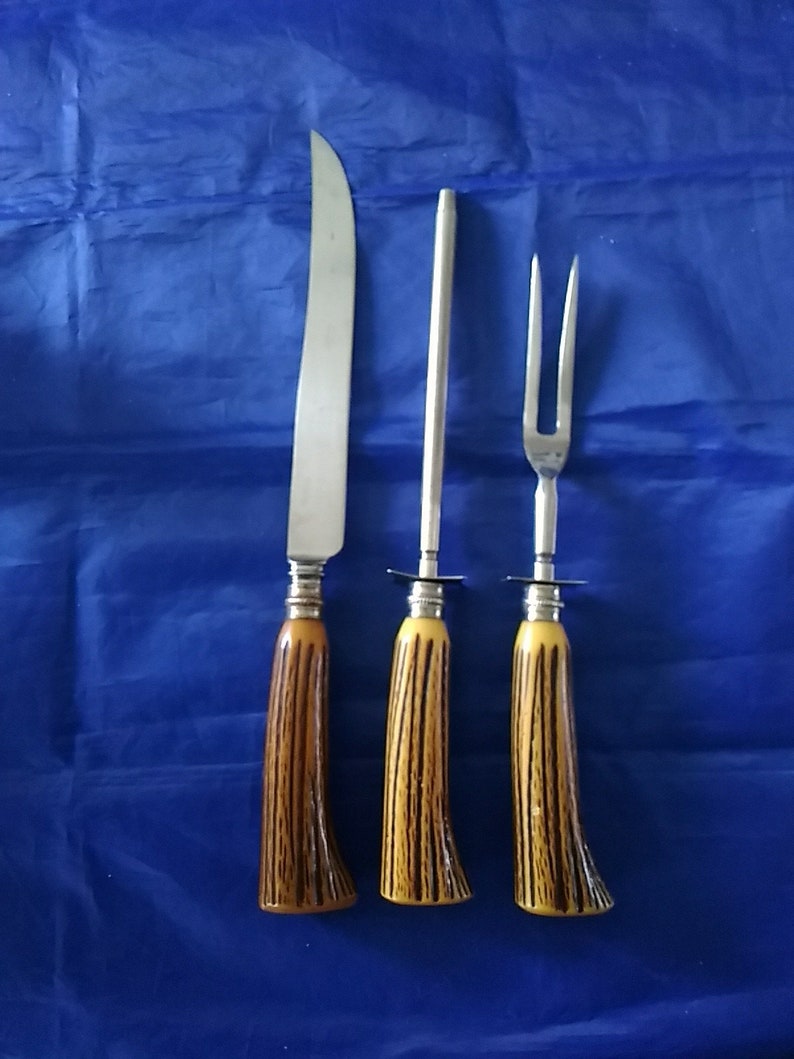 K&ouml;nnte beinhalten: Ein Set aus drei K&uuml;chenutensilien mit braunen und gelben Griffen. Das Set enth&auml;lt ein Messer, eine Fleischgabel und einen Wetzstahl.