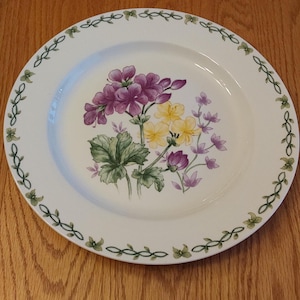 By Thomson Pottery, it is their 12" white chop plate in the purple geranium pattern, with a green vine and leaf rim.  DWS 687