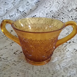 May include: Amber glass sugar bowl with two handles and a detailed embossed pattern.