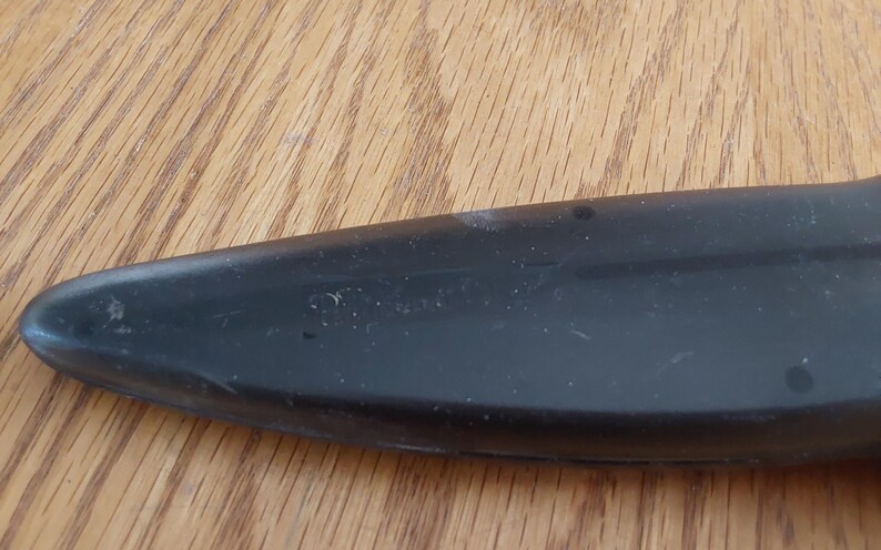 Op de afbeelding: Een close-up van een zwart object met een afgeronde punt. Het object lijkt gemaakt te zijn van een glad materiaal, mogelijk plastic. Het oppervlak vertoont kleine onvolkomenheden en een paar kleine donkere vlekken.