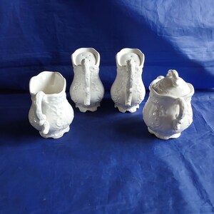 May include: Set of four white ceramic sugar and creamer containers with ornate floral designs. The containers have a vintage look and are perfect for a tea party or special occasion.