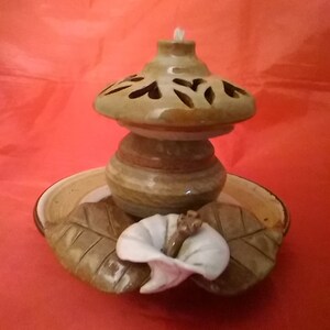 May include: A ceramic oil lamp with a brown and white floral design. The lamp has a round base and a wide, open top with a decorative pattern. The lamp is sitting on a brown and white plate with a floral design.