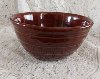 May include: A brown ceramic mixing bowl with a decorative design around the rim. The bowl is sitting on a white lace tablecloth.