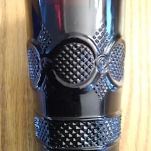 May include: A black glass drinking glass with a diamond pattern around the top and bottom. The glass has a decorative design in the middle.