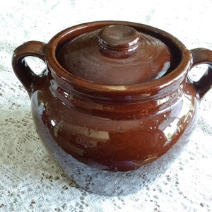 May include: A brown ceramic bean pot with a lid and two handles. The pot has a glossy finish and is slightly speckled.