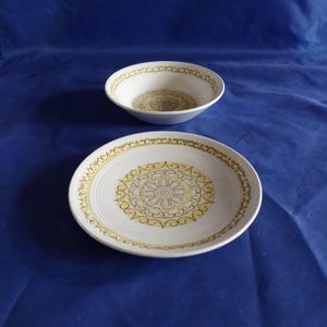 May include: A set of two white ceramic bowls with a yellow and brown floral design. The bowls have a raised rim and a scalloped edge.