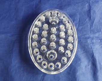 A large glass oval flower and candle frog with 33 holes. The 2 larger holds are for candles and the other 31 holes are for stems.  Vase 408