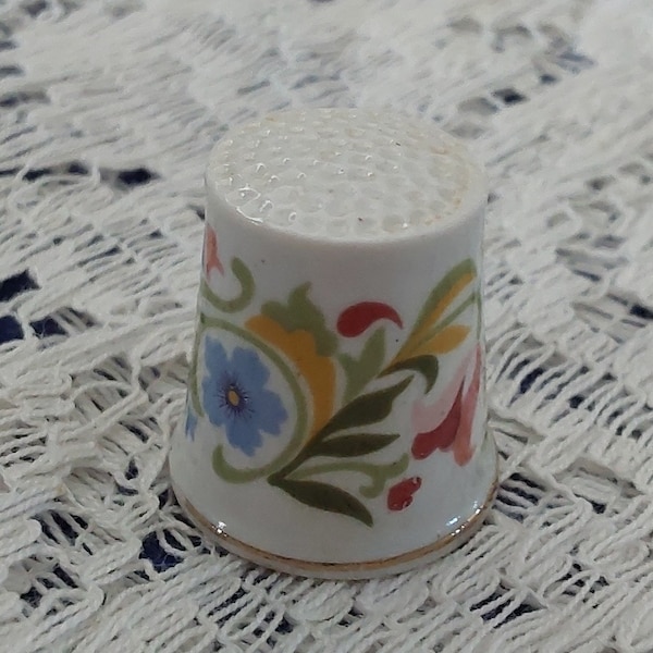 Marked Avon, a white porcelain gold trimmed thimble with a multicolored floral design around it.  Avon C 129