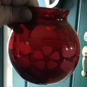 May include: A deep red glass globe with a white floral design. The globe is round and has a smooth surface.