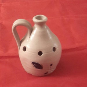 May include: A small, beige ceramic pitcher with a handle and a blue leaf design. The pitcher has several holes around the bottom.