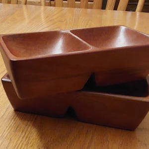 May include: Two wooden serving bowls stacked on top of each other. The bowls are made of dark brown wood and have a rectangular shape. The bowls are divided into two sections.