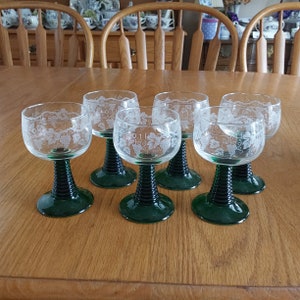 May include: Set of six clear glass wine glasses with etched grape designs and green stems. The glasses have a swirling pattern on the stems.