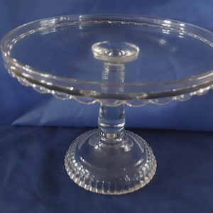 May include: A clear glass cake stand with a scalloped edge and a fluted base.