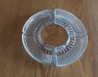 Puede incluir: Plato de servir de vidrio transparente con cuatro secciones, ideal para aperitivos o entremeses. El plato tiene forma circular con un diseño acanalado y está colocado sobre una superficie de madera.