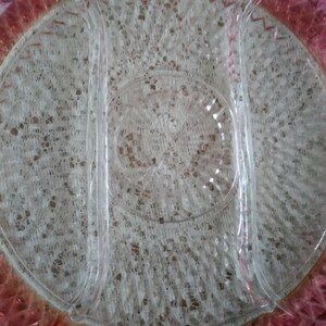 May include: A clear glass serving dish with three sections. The dish has a pink rim with a gold accent. The dish is on a white lace tablecloth.